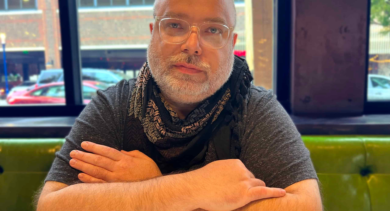 Jon Rezin, mix and mastering engineer and the founder of Crate, seated in a booth by a street-facing window, arms folded, wearing glasses and a patterned scarf.